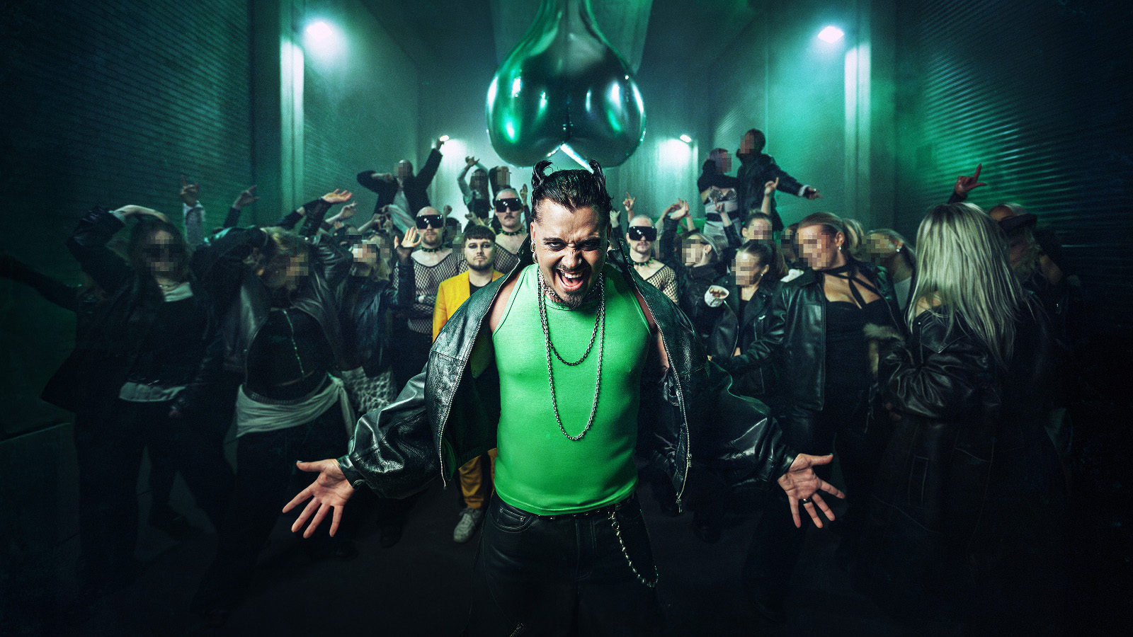 Kuvassa on keskellä Käärijä vihreässä puserossa ja mustassa nahkatakissa. Taustalla on joukko ihmisiä ja valoja ohjattuna heihin.
