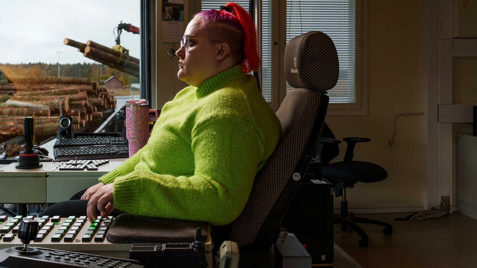 Kuvassa on nuori nainen vaalen vihreässä puserossa istumassa sivuttain nojatuolissa ja hän näppäilee kädellään alla olevia näppäimiä. Taustalla näkyy ruskeaa maisemaa.