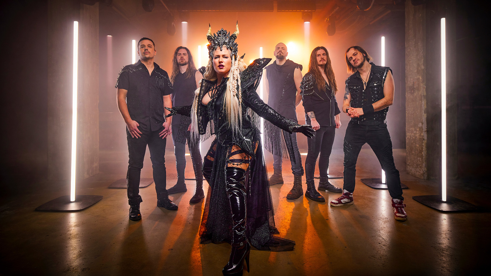 Kuvassa on edessä yhtyeen naissolisti mustassa puvussa, jossa on siipimäiset olkapäät ja päässä kruunu. Taustalla on viisi yhtyeen miesjäsentä seisomassa mustissa vaatteissa. Taustalla on pystyledvaloja ja seinien värit violettia ja oranssia.