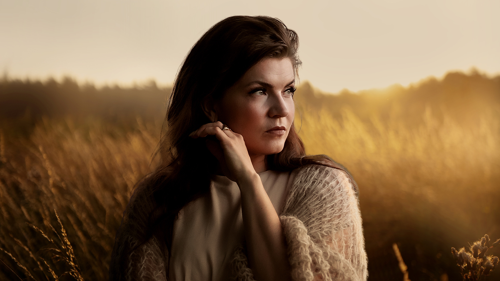 Kuvassa on Suvi Teräsniska puolivartalokuvassa ja hän katsoo oikealle. Taustalla on auringonlaskun kellertävää ja viljapelto, jossa on usvaa.