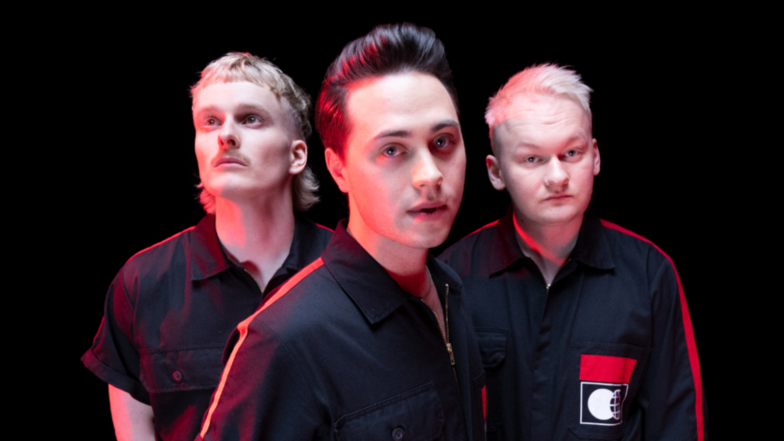 Kuvassa ovat KUUMAA yhtyeen kolme jäsentä puolivartalokuvassa. He ovat tiiviisti ryhmänä ja etummaisena on Johannes Brotherus.  Kaikilla on mustat t-paidat, joissa on punaiset raidat reunoissa.  Tausta on musta.