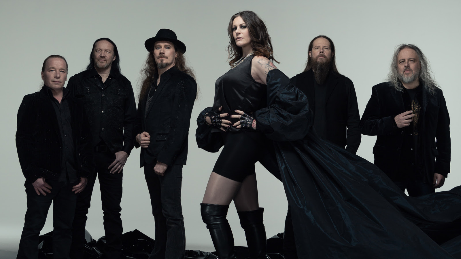 Kuvassa on seisomassa Nightwishin viisi miesjäsentä taaempana ja naisjäsen keskellä edessä. Kaikilla on mustat vaatteen päällään. Tausta on harmaa.