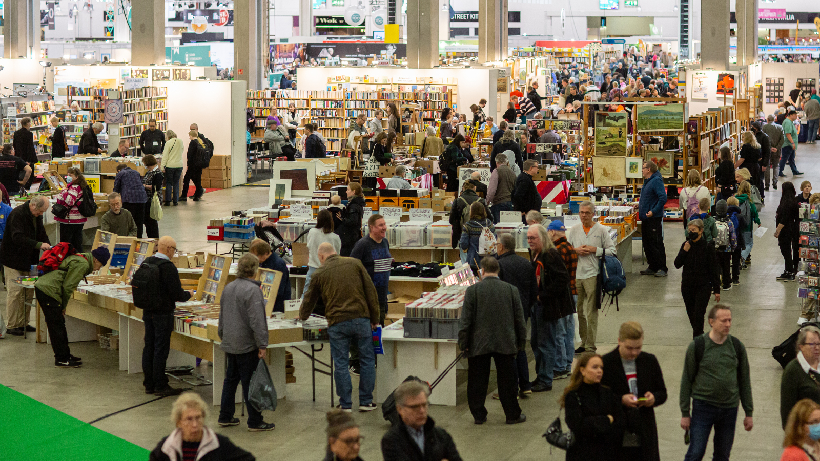 Kuvassa on Helsingin Kirjamessujen yleisöä kuvattuna ylhäältä päin ja siinä on ihmisiä kiertelemässä kirjapöytiä. 