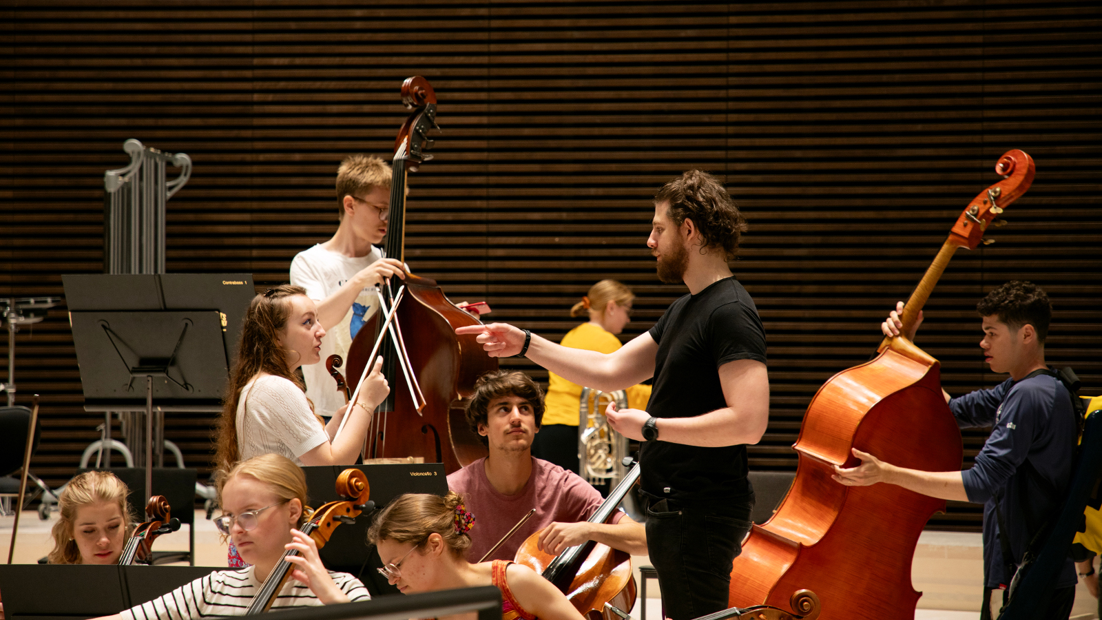 Kuvassa on Sibelius-Akatemian nuoria soittajia soittoharjoituksissa. Keskellä seisoo nuori nainen ja miesvalkoisissa t-paidoissa ja heitä vastapäätä seisoo mustissa vaatteissa kapellimestari ohjaamassa heitä. Takana on sellon soittaja.