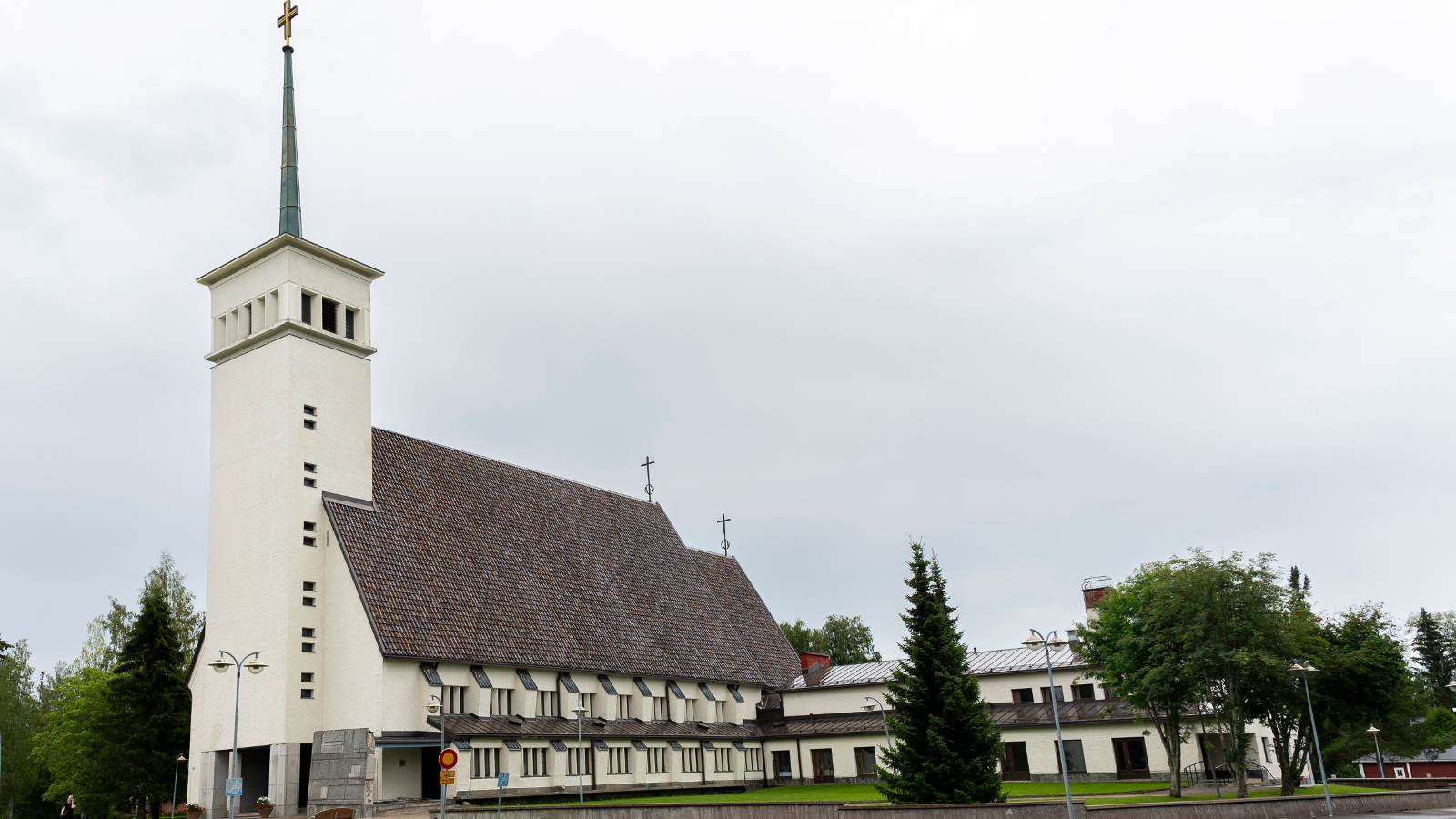 Kuvassa on Teuvan kirkko, jossa on edessä neliömäinen torni, jonka yläosassa on ikkunoita. Katto on tumma tiilikatto, joka on jyrkkä ja sen alla on kaksi riviä ikkunoita. Kirkon väri on vaalea.