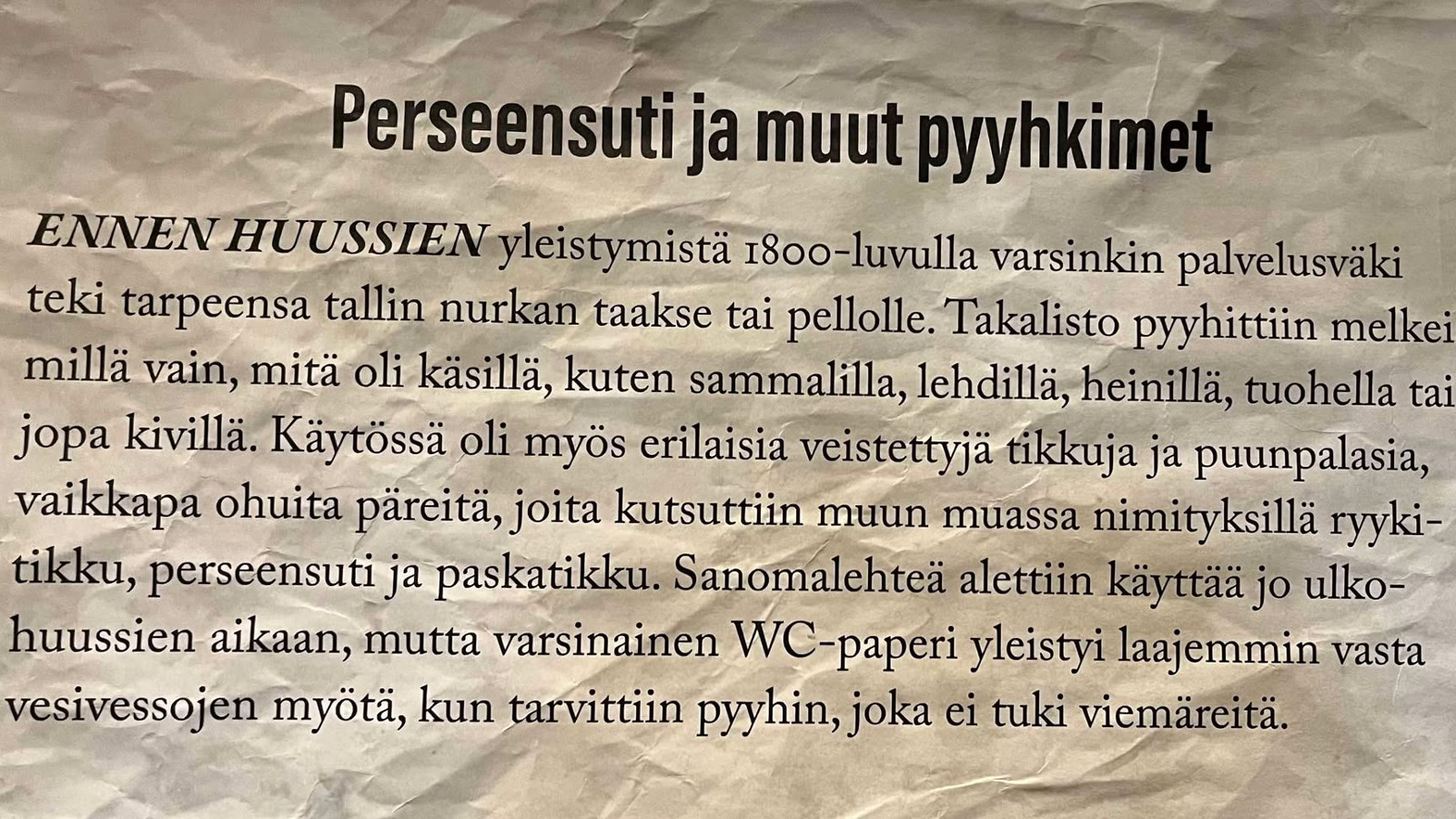 Kuvassa on ruttuista harmaata paperia, jossa on otsikkona Pereensuti ja muut pyyhkimet. Tekstissä on historia takapuolen pyyhkimisestä ennen WC-paperia.