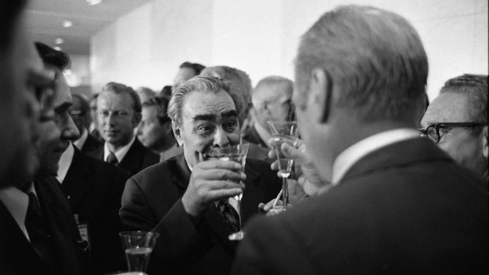 Kuvassa on coktail-tilaisuus, jossa keskellä on Leonid Brezhnev nostamassa maljaa ja häntä vastapäätä seisoo selin Gerald ford.  Kuvan helnkilöt ovat puolivartalokuvassa.