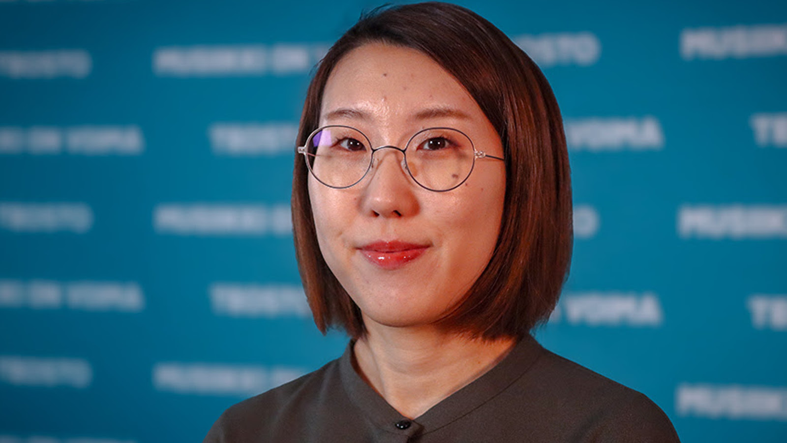 Kuvassa on Mioko Yokoyama kasvokuvassa. Hänellä on pyöreät silmälasit ja ruskea suora tukka. Taustalla on sinistä seinää ja siinä on valkoista himmeää tekstiä.