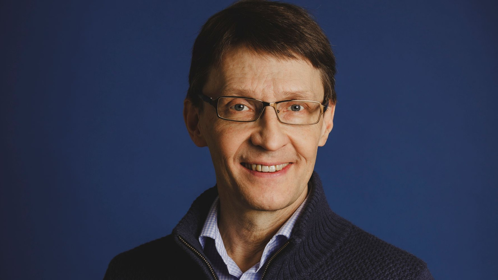 Kuvassa on Markus Nummi puolivartalokuvassa. Hänellä on tummansininen pusero ja vaalea paita. Tausta on tummansininen.